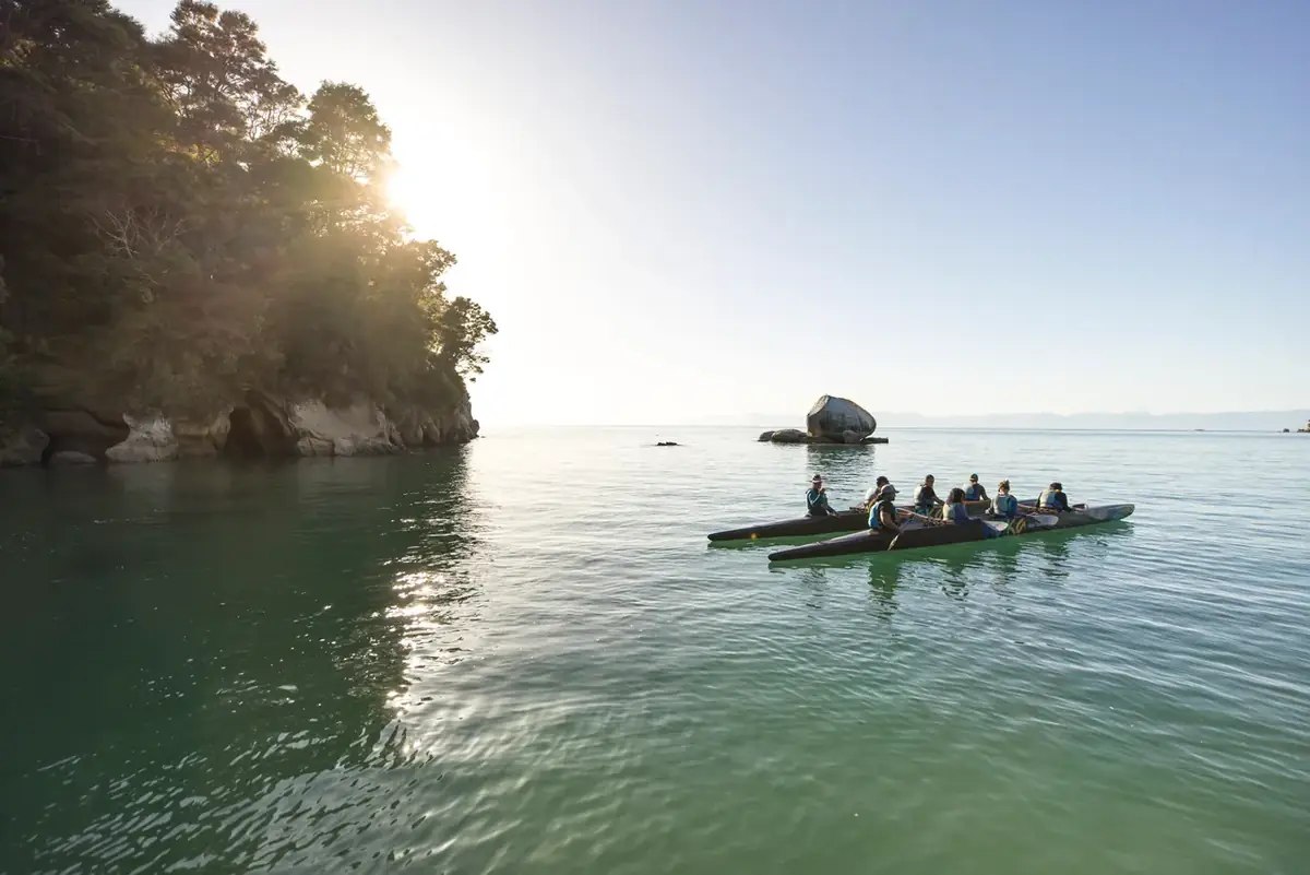 Paddlers on calm water beneath a rock island on the Abel Tasman coast