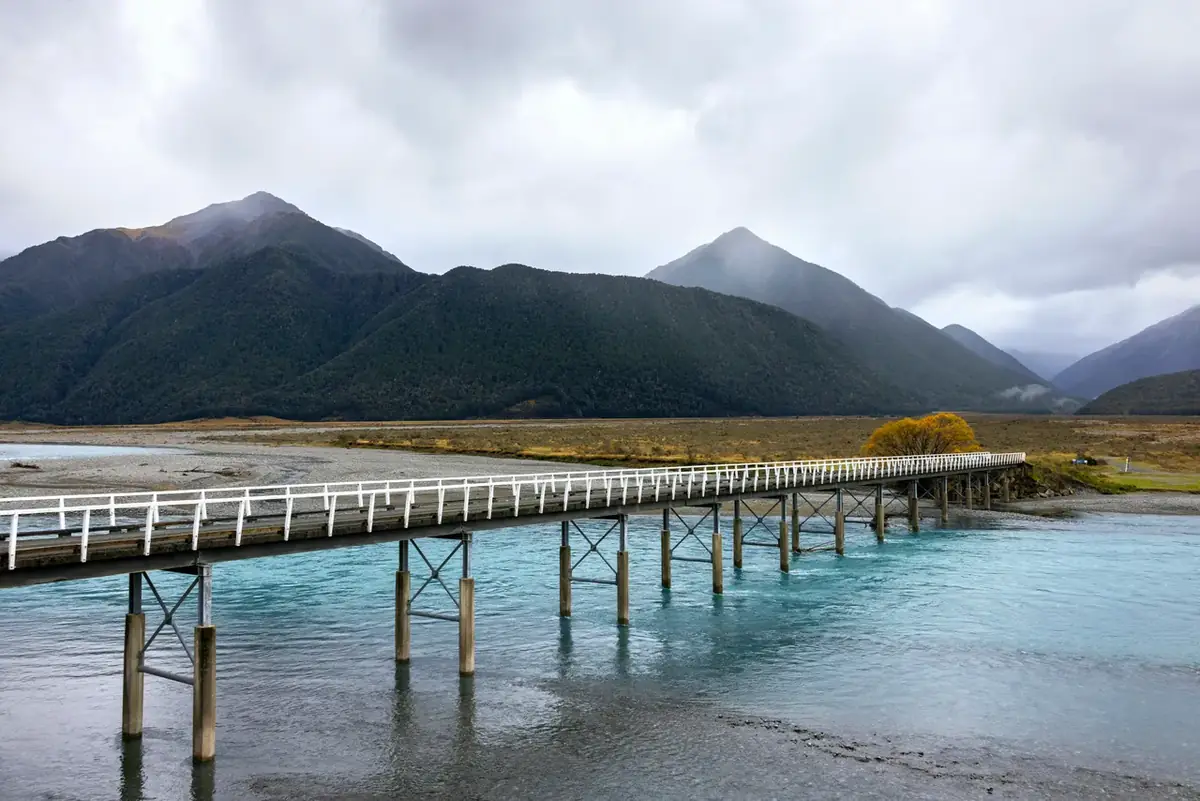 A long timber bridge crossing a turquoise braided river on the road into the Southern Alps