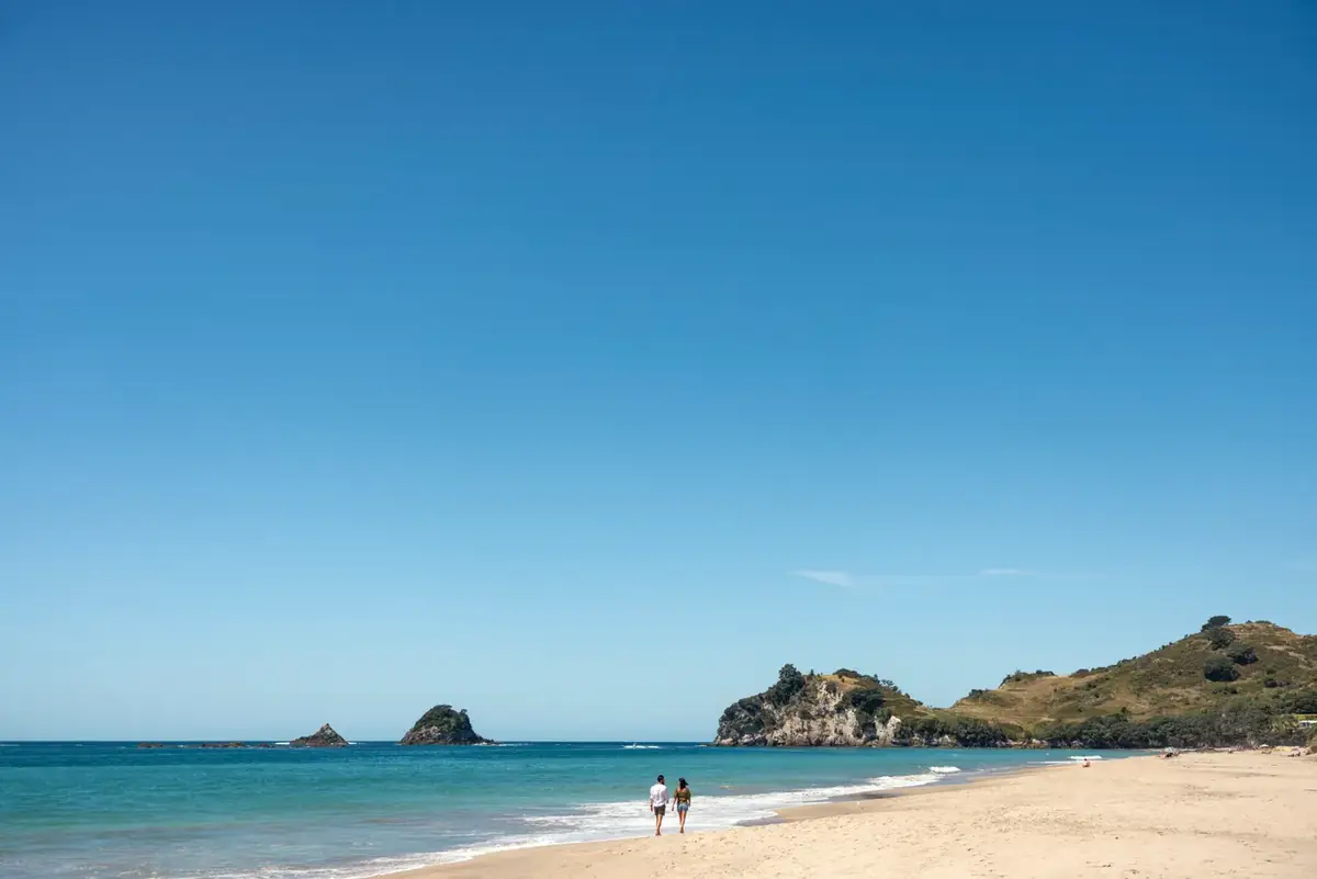 Two people walking the golden sand at Hahei Beach on the Coromandel with islands offshore