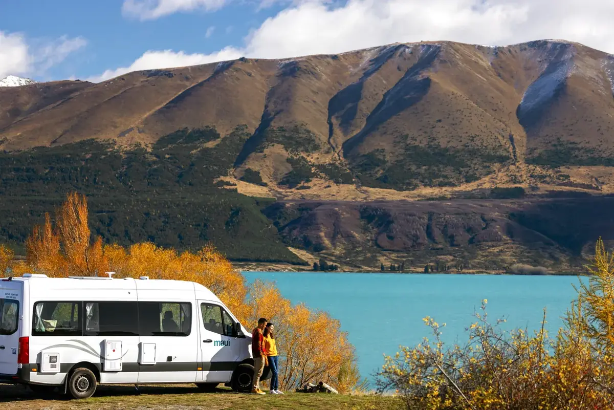 Travellers beside a campervan on the shore of Lake Pukaki