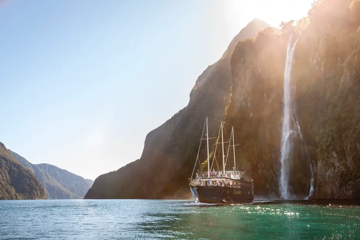 A cruise ship dwarfed by a waterfall and the cliffs of Milford Sound