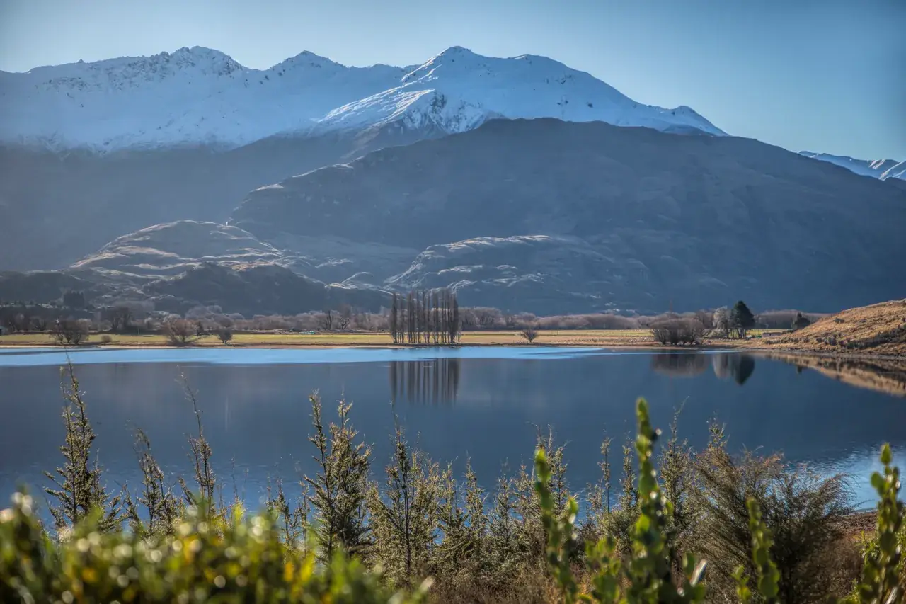 Snow-covered peaks above a still high-country lake with poplars along the shore