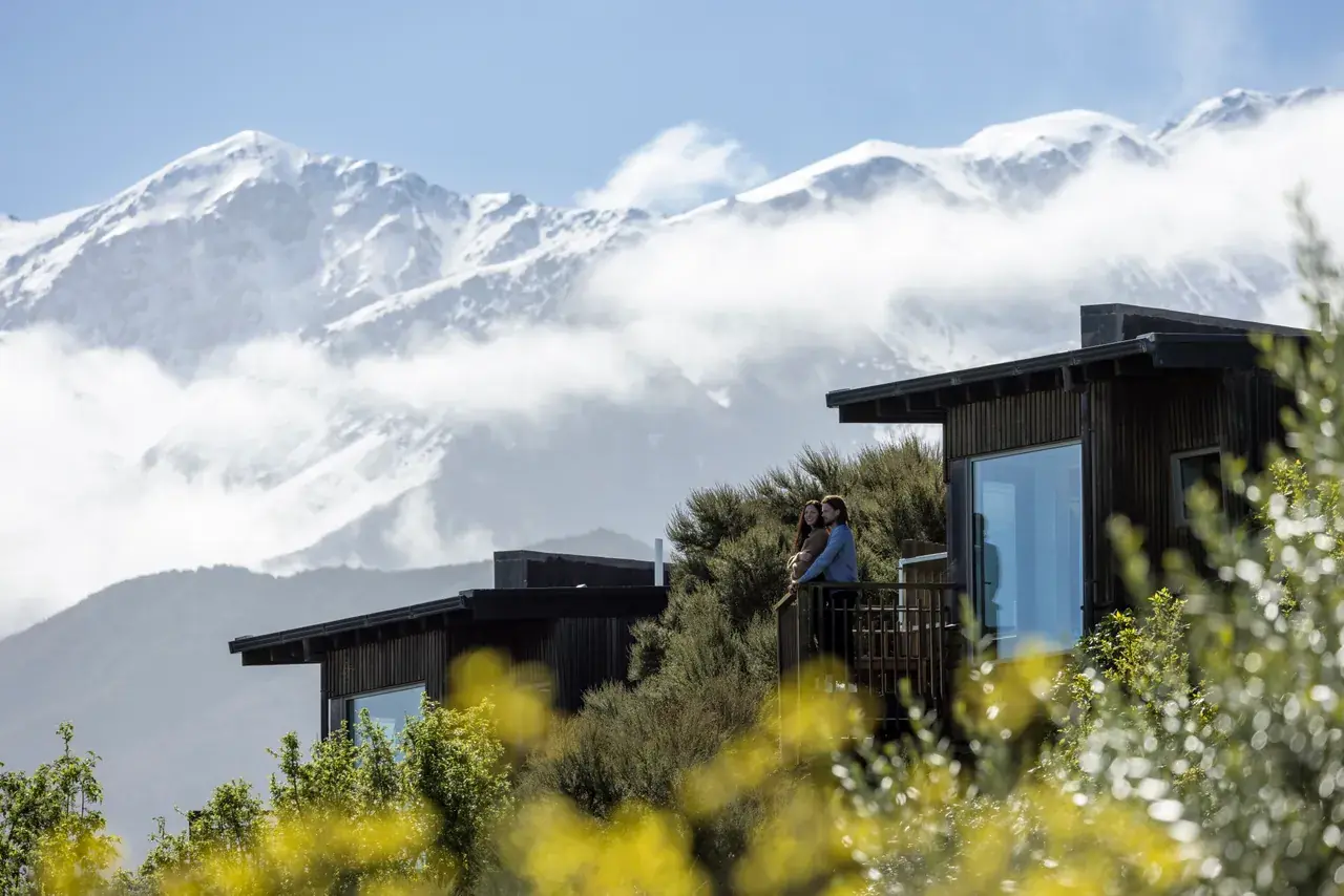 Lodge cabins on a hillside with snow-capped mountains behind
