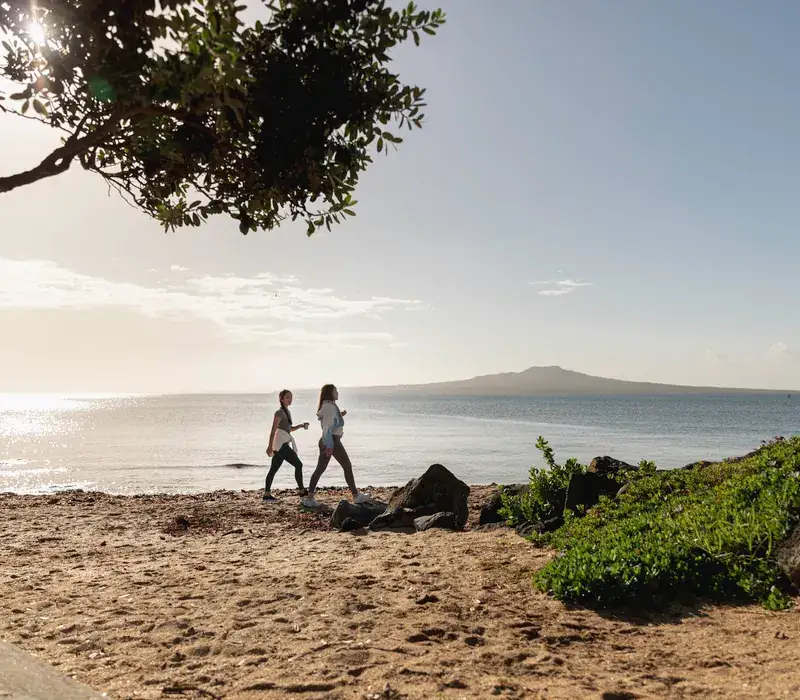 Morning walkers on Takapuna Beach with Rangitoto Island across the water