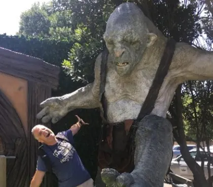 A visitor posing beneath a huge sculpted troll on a Middle-earth themed tour