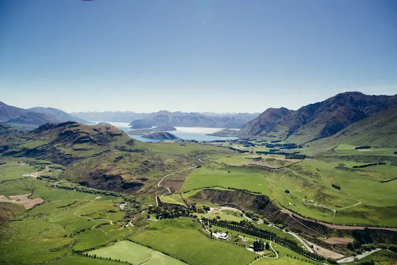 Aerial view over green valleys towards Lake Wanaka and the Southern Alps