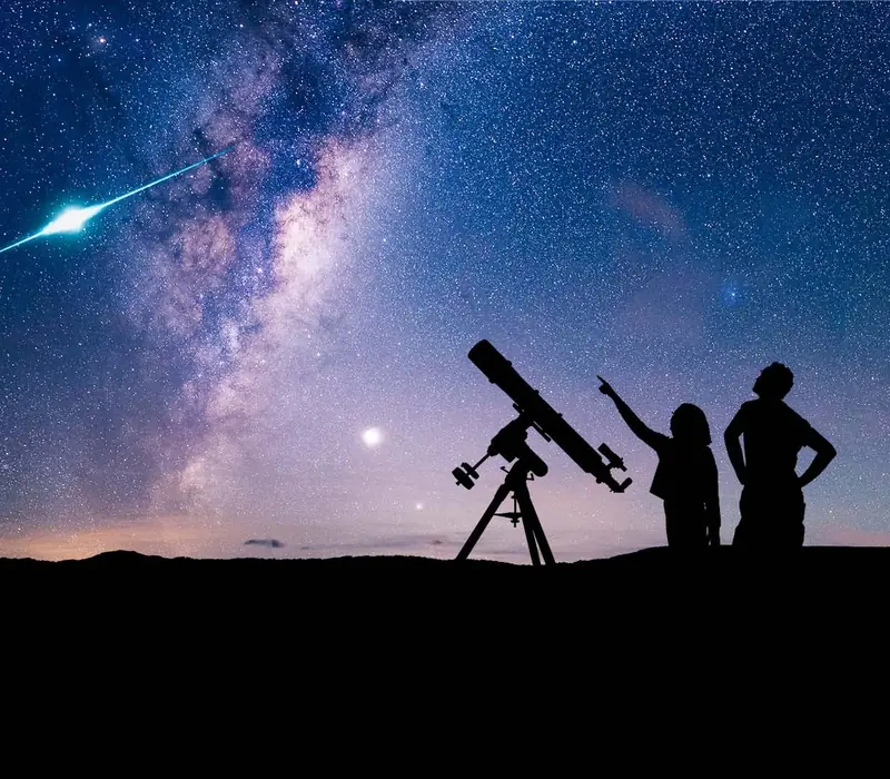 Stargazers and a telescope silhouetted beneath the Milky Way