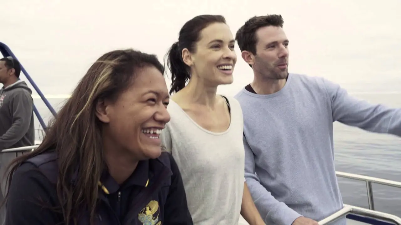 Three passengers smiling at the rail of a whale watching boat off Kaikoura